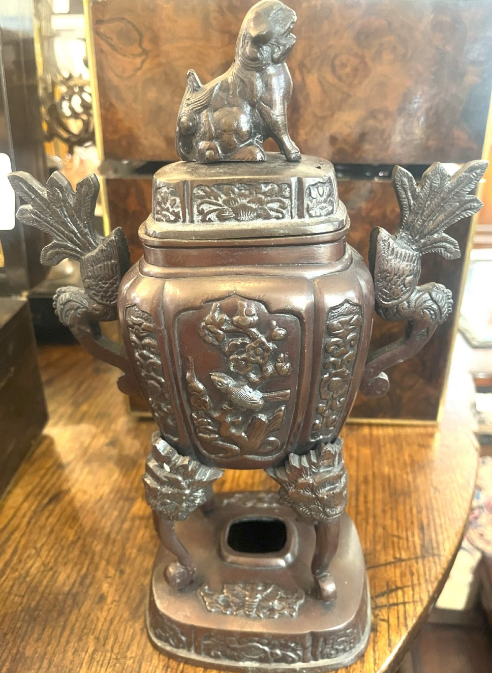 A cast dark bronze Japanese incense burner featuring a shishi guardian dog finial on the lid, floral relief panels, phoenix handles, and beast-head legs.