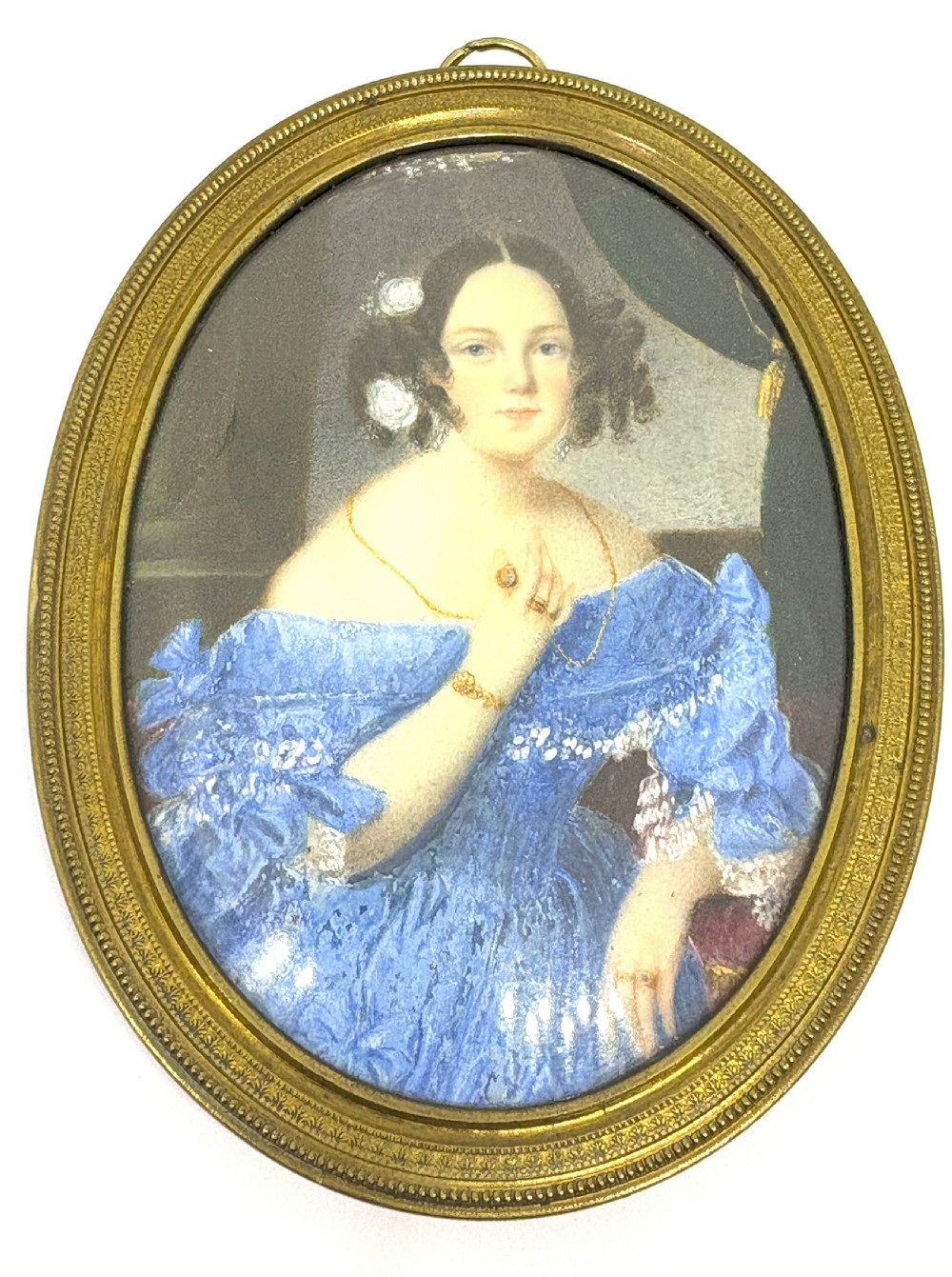 An oval 19th-century French portrait miniature depicting a woman in a blue lace gown enclosed in a beaded gilt metal frame.