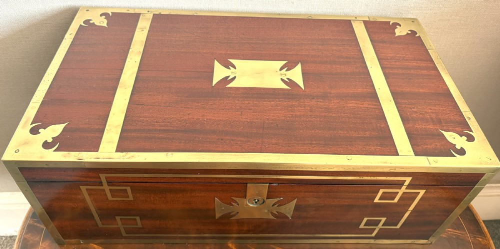 A rectangular mahogany writing slope box featuring flush brass corner brackets, brass strapping, and a central brass inlay.