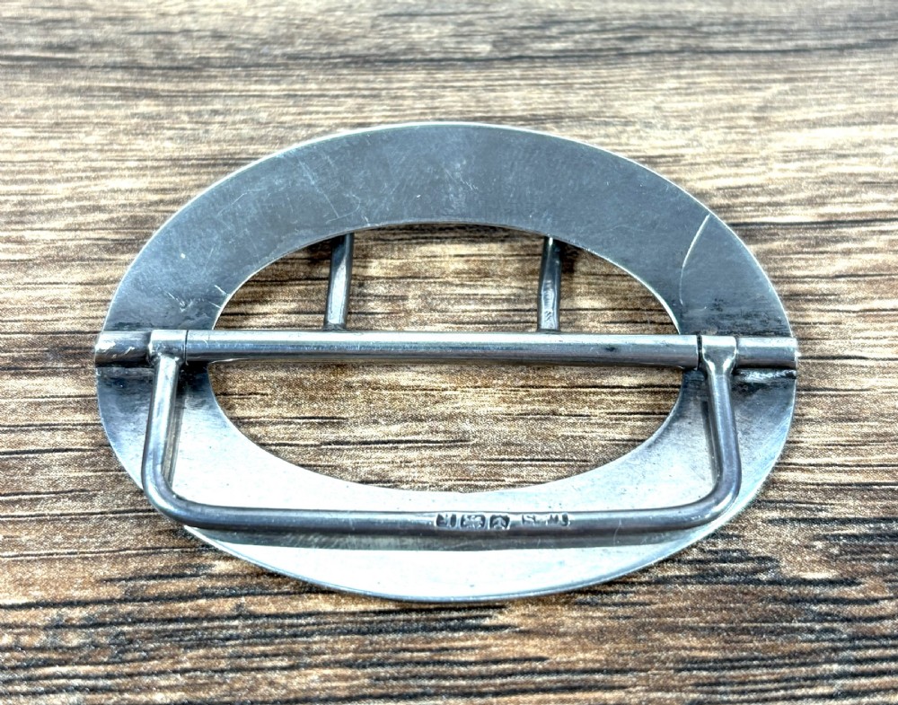 An oval silver belt buckle featuring a light blue guilloche enamel border with foliate scroll engraving and a double central prong. View III