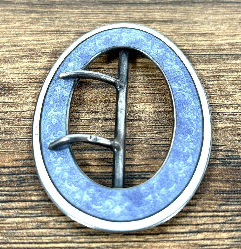 An oval silver belt buckle featuring a light blue guilloche enamel border with foliate scroll engraving and a double central prong. View IV