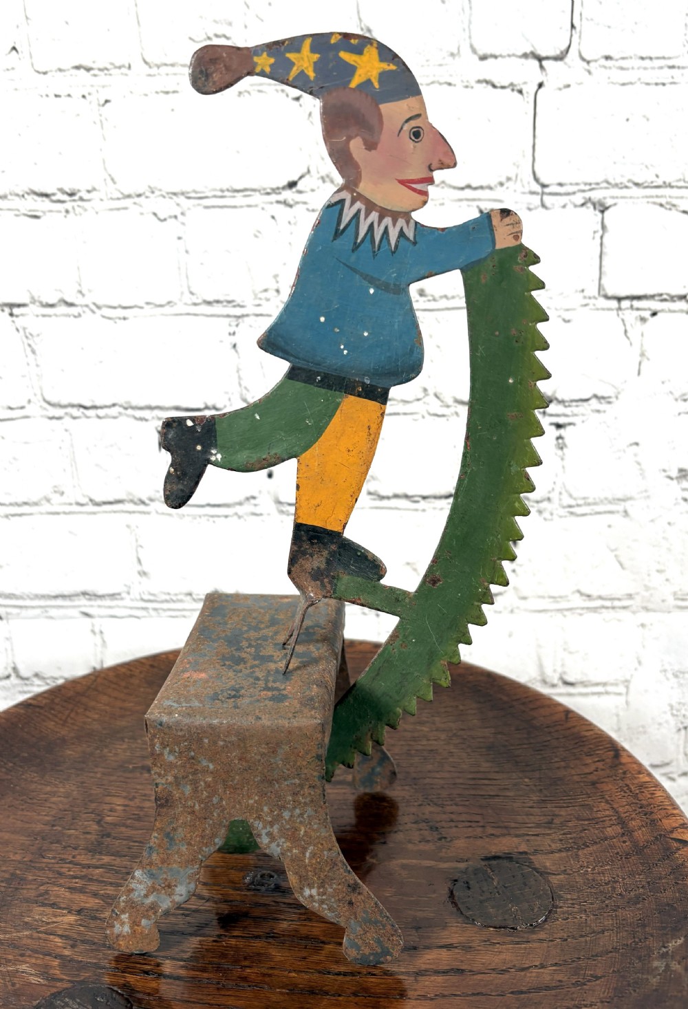 A painted sheet-metal kinetic balance toy featuring a jester figure in a starred hat balancing on a rusted iron pedestal. View III
