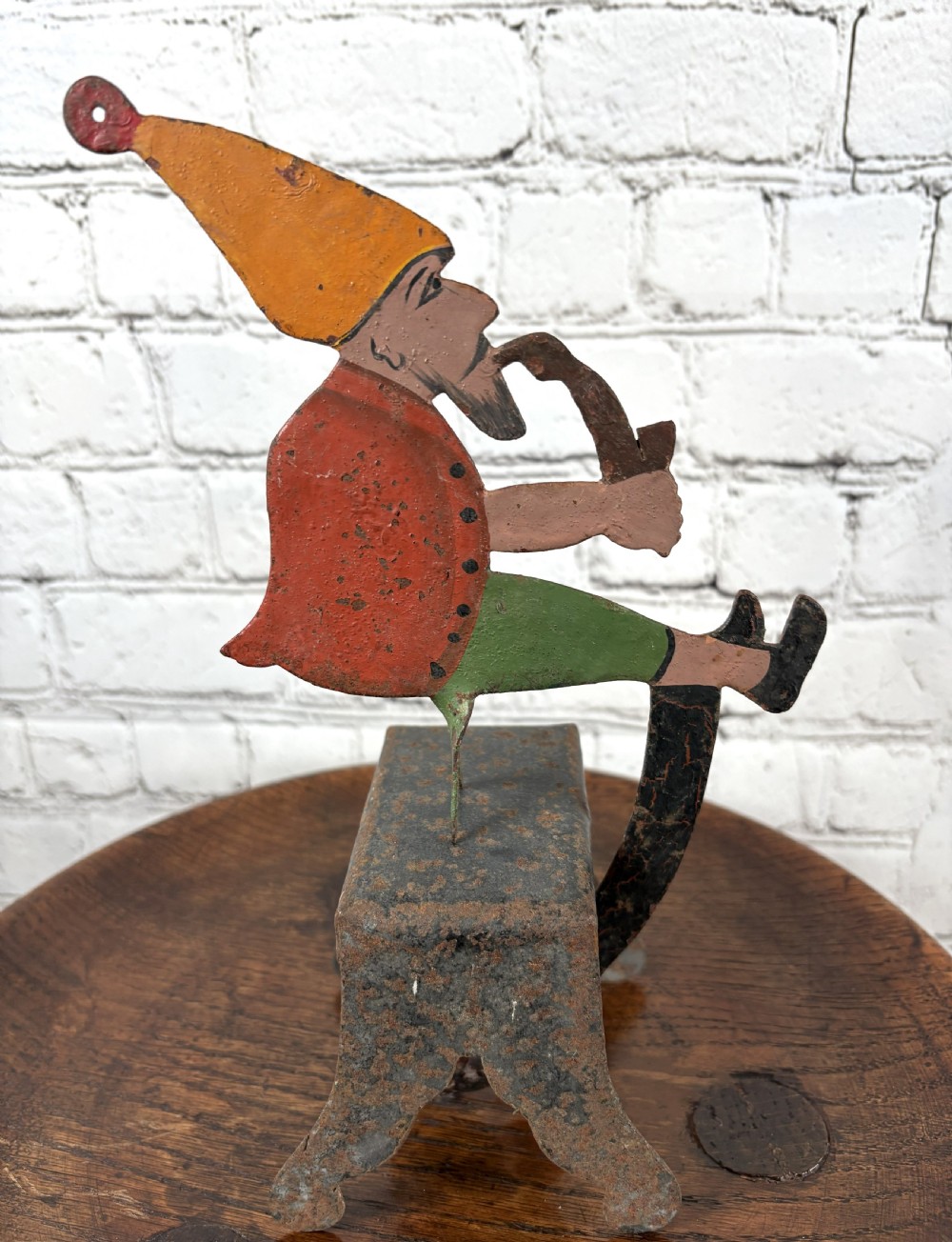 A painted metal balance toy depicting a figure in an orange hat smoking a pipe, mounted on an iron base with a counterweight.