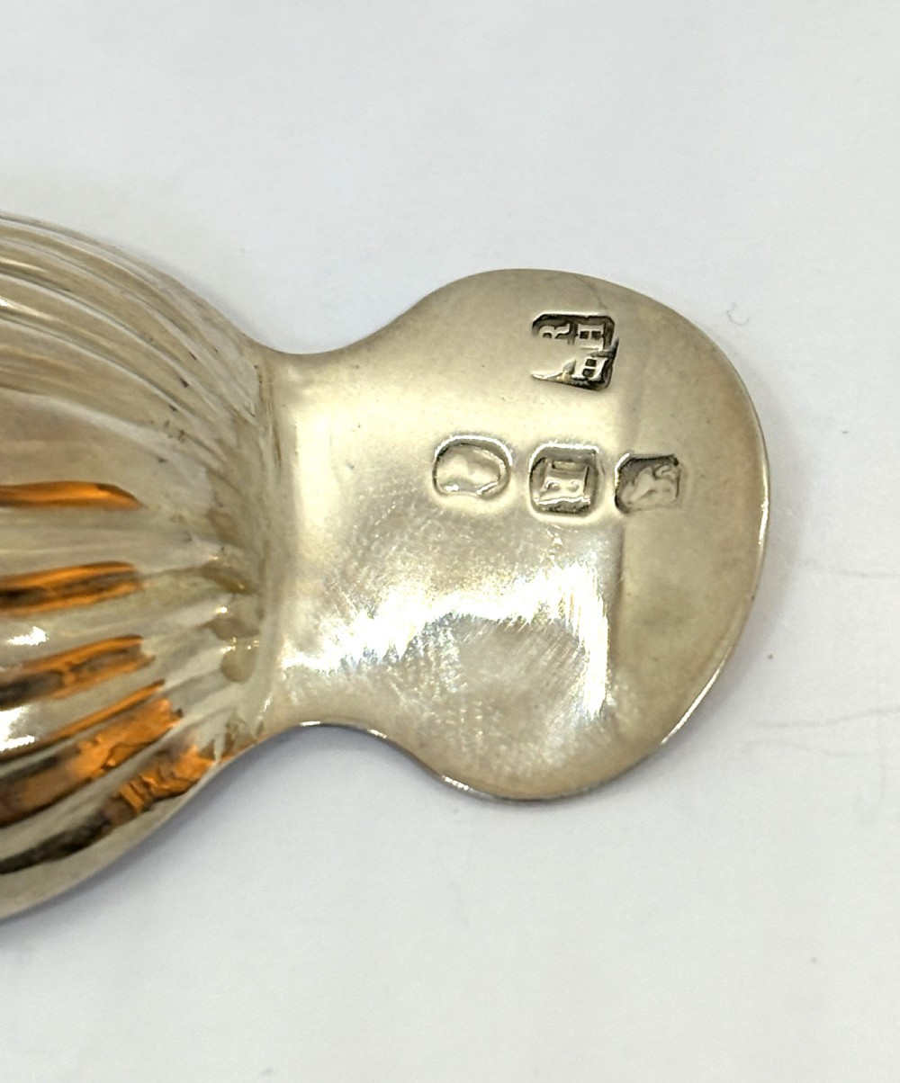 A Georgian sterling silver caddy spoon featuring an acorn-form fluted bowl and stamped British hallmarks on the short handle. View V