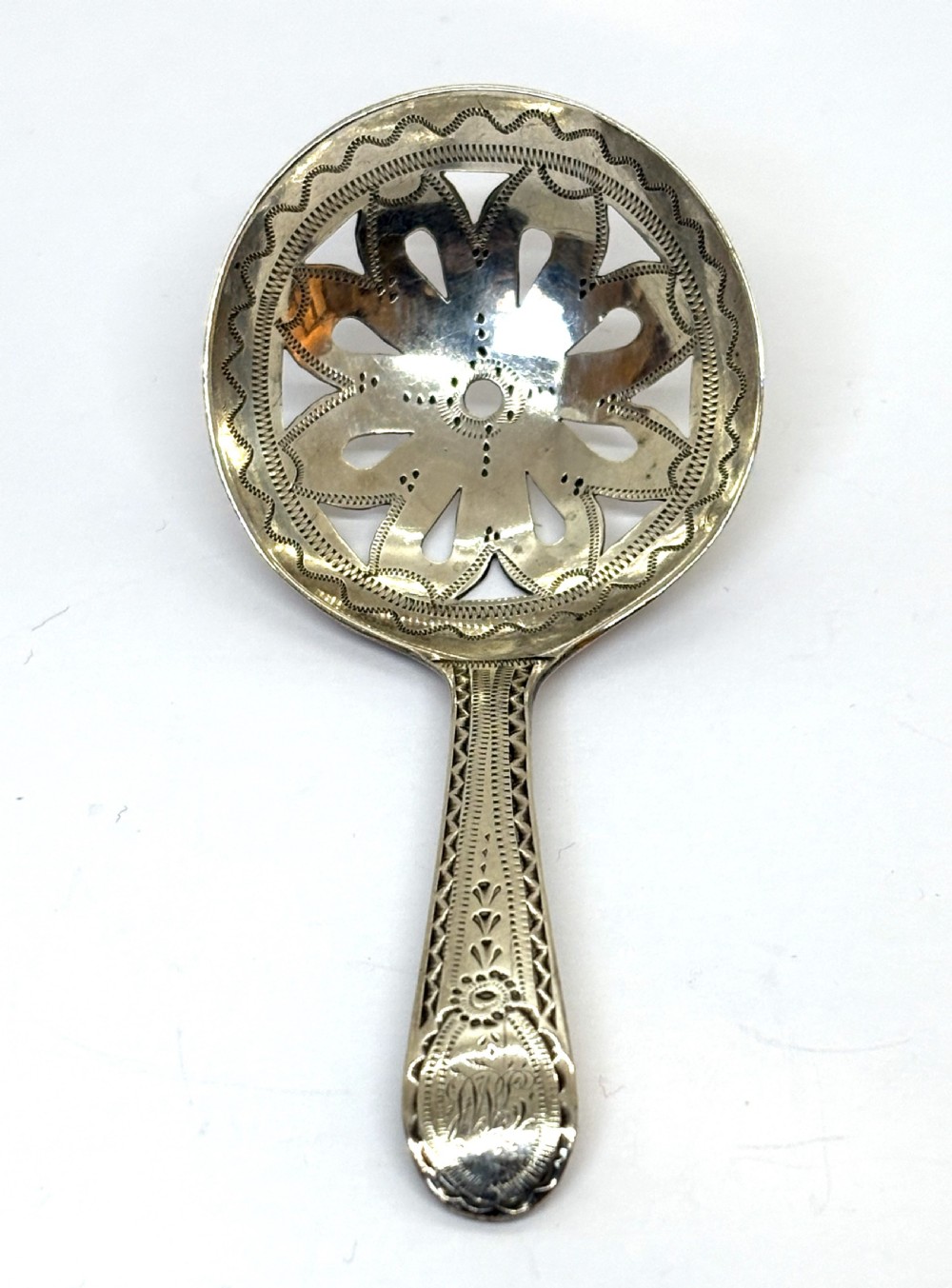 A Georgian sterling silver caddy spoon dating from 1799 with a circular pierced floral bowl and bright-cut engraved handle.
