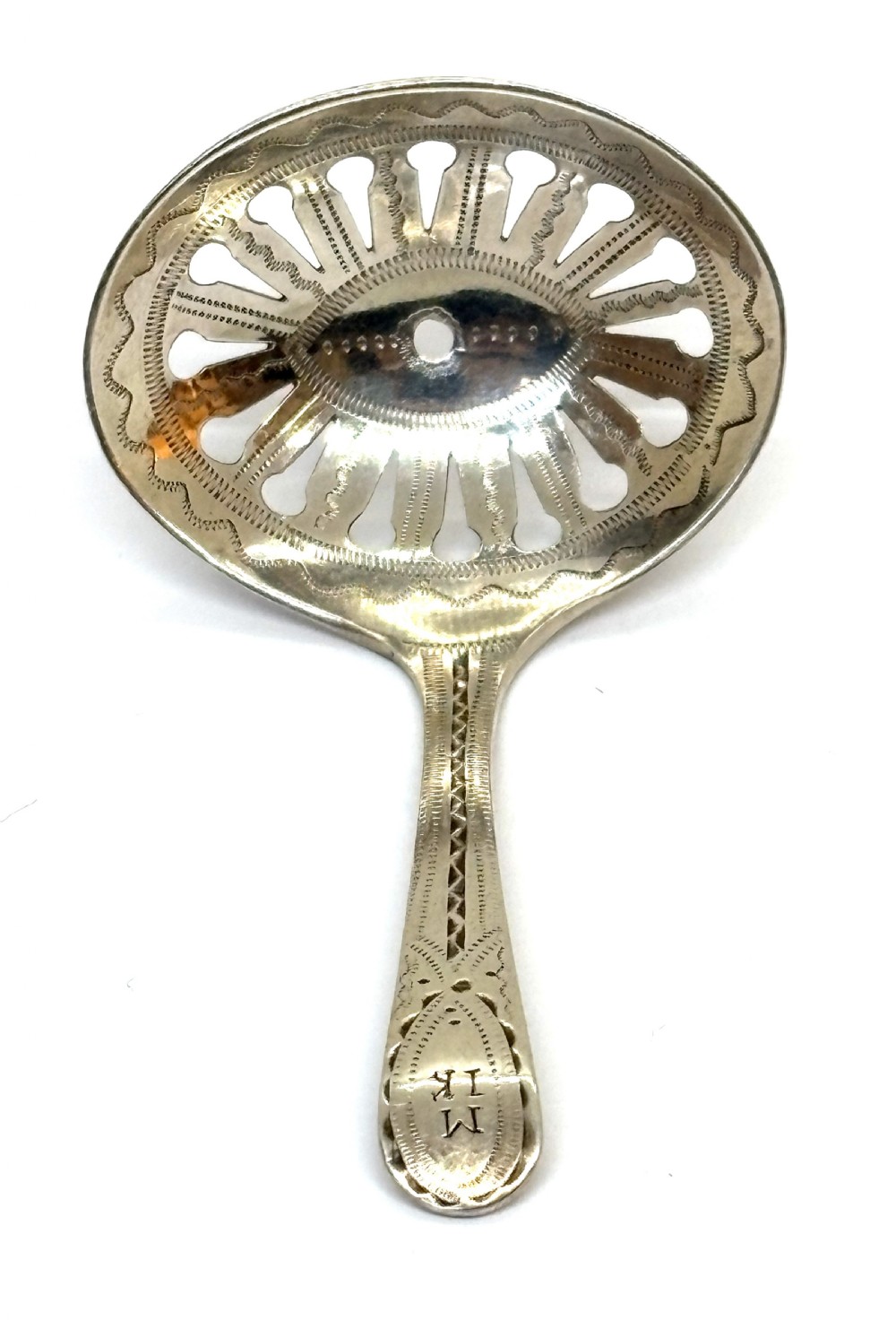 A Georgian sterling silver caddy spoon featuring a pierced oval bowl with engraved geometric detailing and a monogrammed handle.
