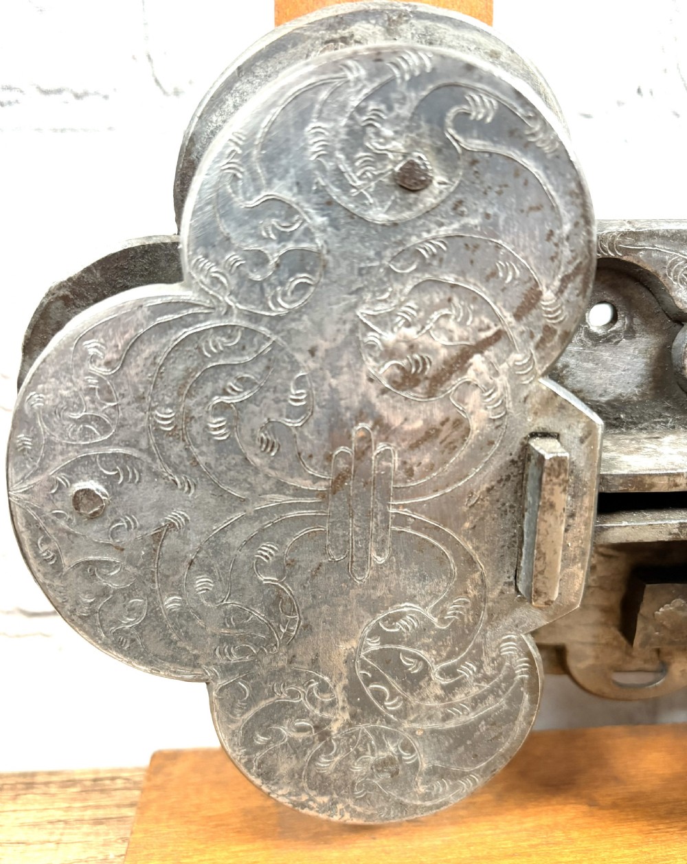 A 17th-century French wrought iron twin spring bolt door lock featuring detailed foliate scroll engravings and lobed metal plates, mounted on a light timber display stand. View II