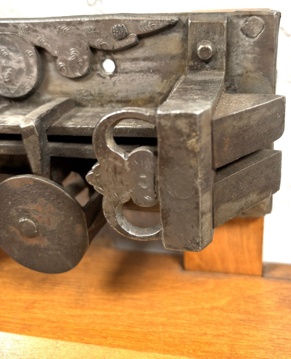A 17th-century French wrought iron twin spring bolt door lock featuring detailed foliate scroll engravings and lobed metal plates, mounted on a light timber display stand. View IV