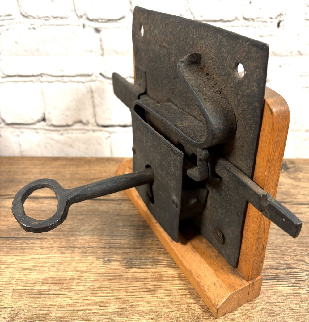 A 16th-century hand-forged wrought iron rim lock mechanism with a large iron key inserted into the lock plate. View IV