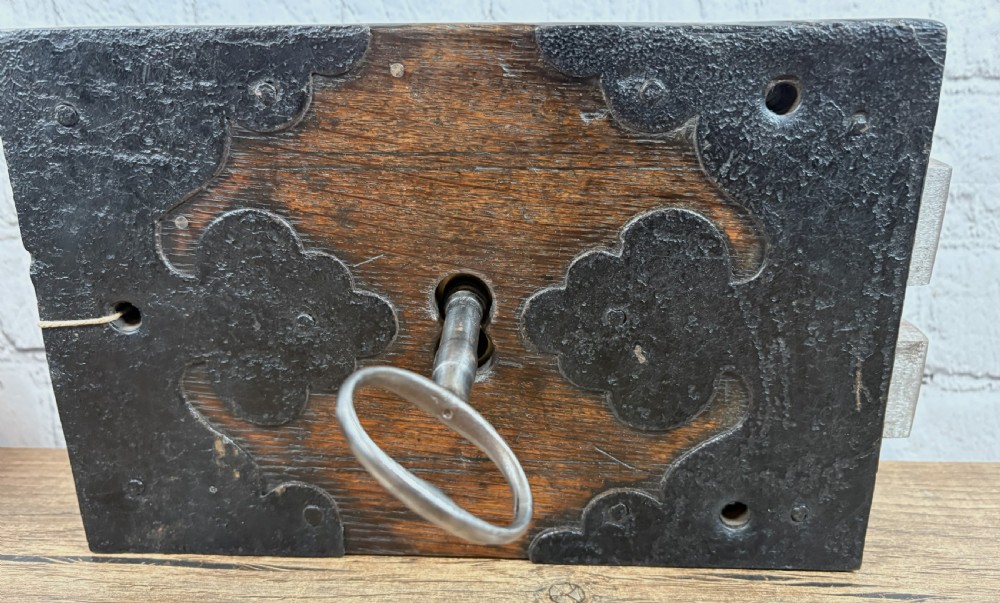 A 19th-century rectangular oak cased stock lock with decorative black iron corner plates, a central keyhole, and an inserted iron key.