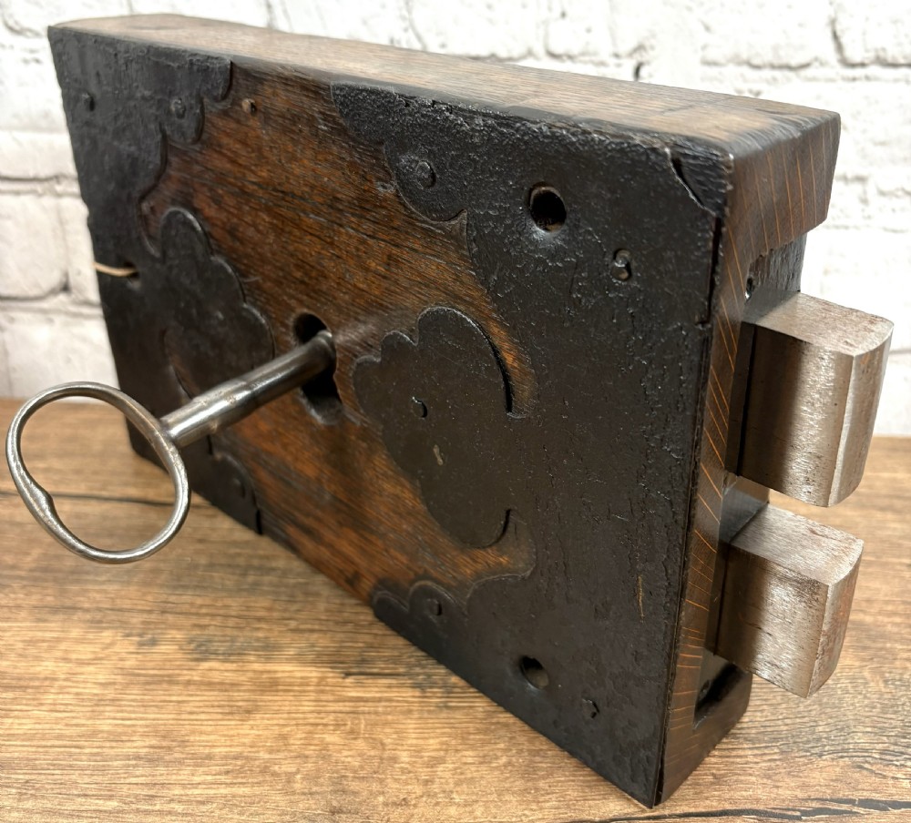 A 19th-century rectangular oak cased stock lock with decorative black iron corner plates, a central keyhole, and an inserted iron key. View II