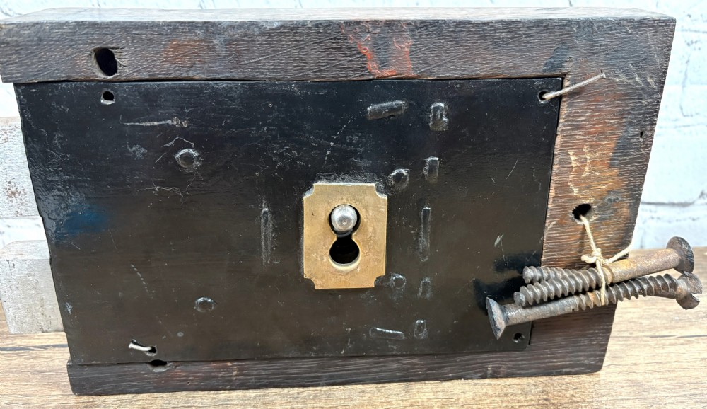 A 19th-century rectangular oak cased stock lock with decorative black iron corner plates, a central keyhole, and an inserted iron key. View III