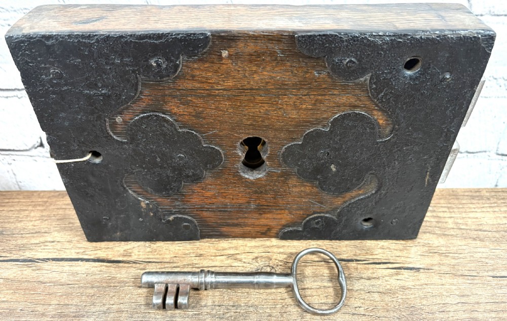 A 19th-century rectangular oak cased stock lock with decorative black iron corner plates, a central keyhole, and an inserted iron key. View IV