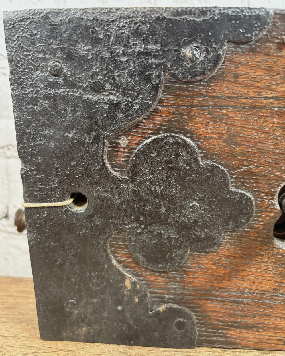 A 19th-century rectangular oak cased stock lock with decorative black iron corner plates, a central keyhole, and an inserted iron key. View VI