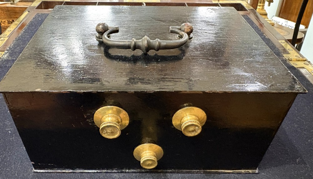 A rectangular black iron safe box featuring a top metal handle and three brass combination dials on the front.