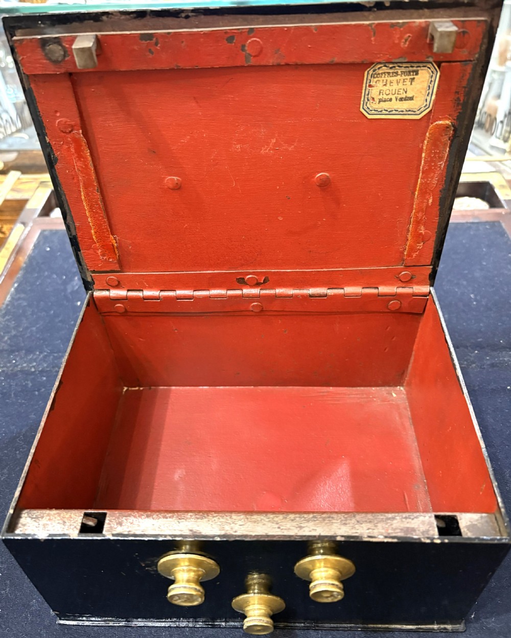 A rectangular black iron safe box featuring a top metal handle and three brass combination dials on the front. View V