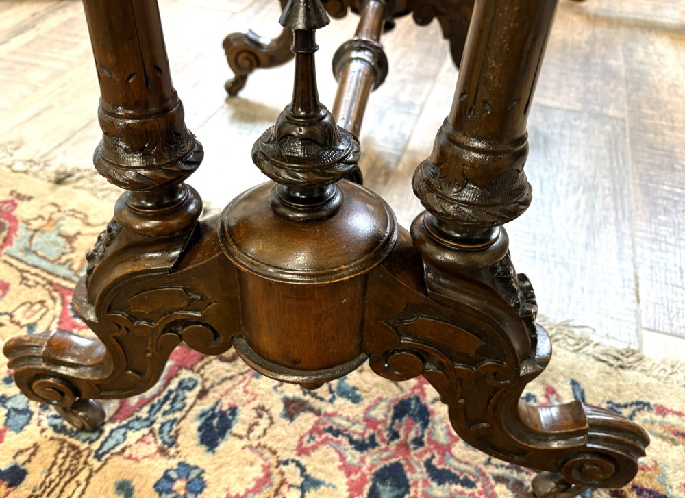 An oval Victorian burr walnut stretcher table featuring marquetry inlays, turned twin-column supports, a central stretcher rail, and carved legs with castors. View VII