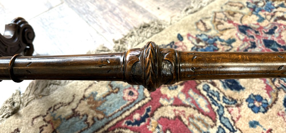 An oval Victorian burr walnut stretcher table featuring marquetry inlays, turned twin-column supports, a central stretcher rail, and carved legs with castors. View VIII