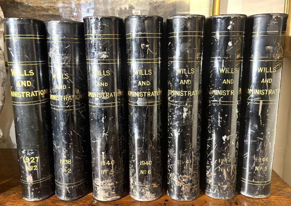 A set of seven black painted metal cylindrical toleware tins featuring gold-lettered spines reading Wills and Administrations alongside early twentieth-century dates.