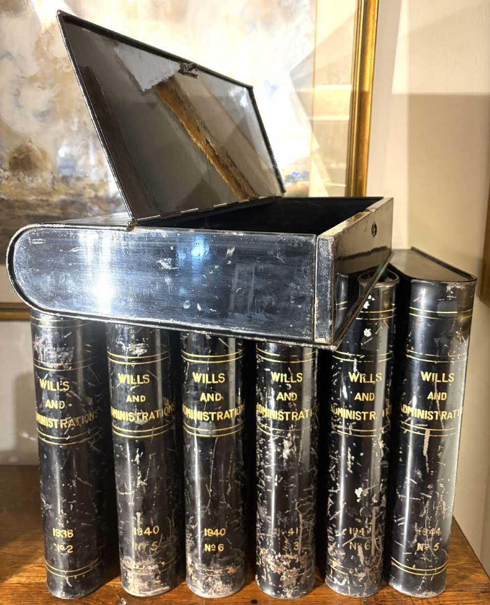 A set of seven black painted metal cylindrical toleware tins featuring gold-lettered spines reading Wills and Administrations alongside early twentieth-century dates. View II