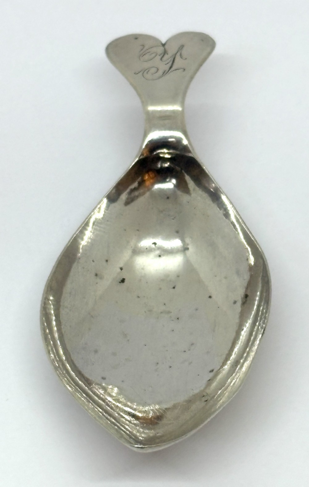 An antique Georgian sterling silver tea caddy spoon featuring a tear-shaped bowl and a flared handle with engraved monogram lettering.