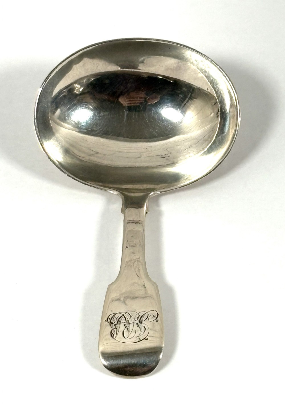 A Georgian sterling silver tea caddy spoon featuring a broad oval bowl and a flat handle with an engraved monogram.