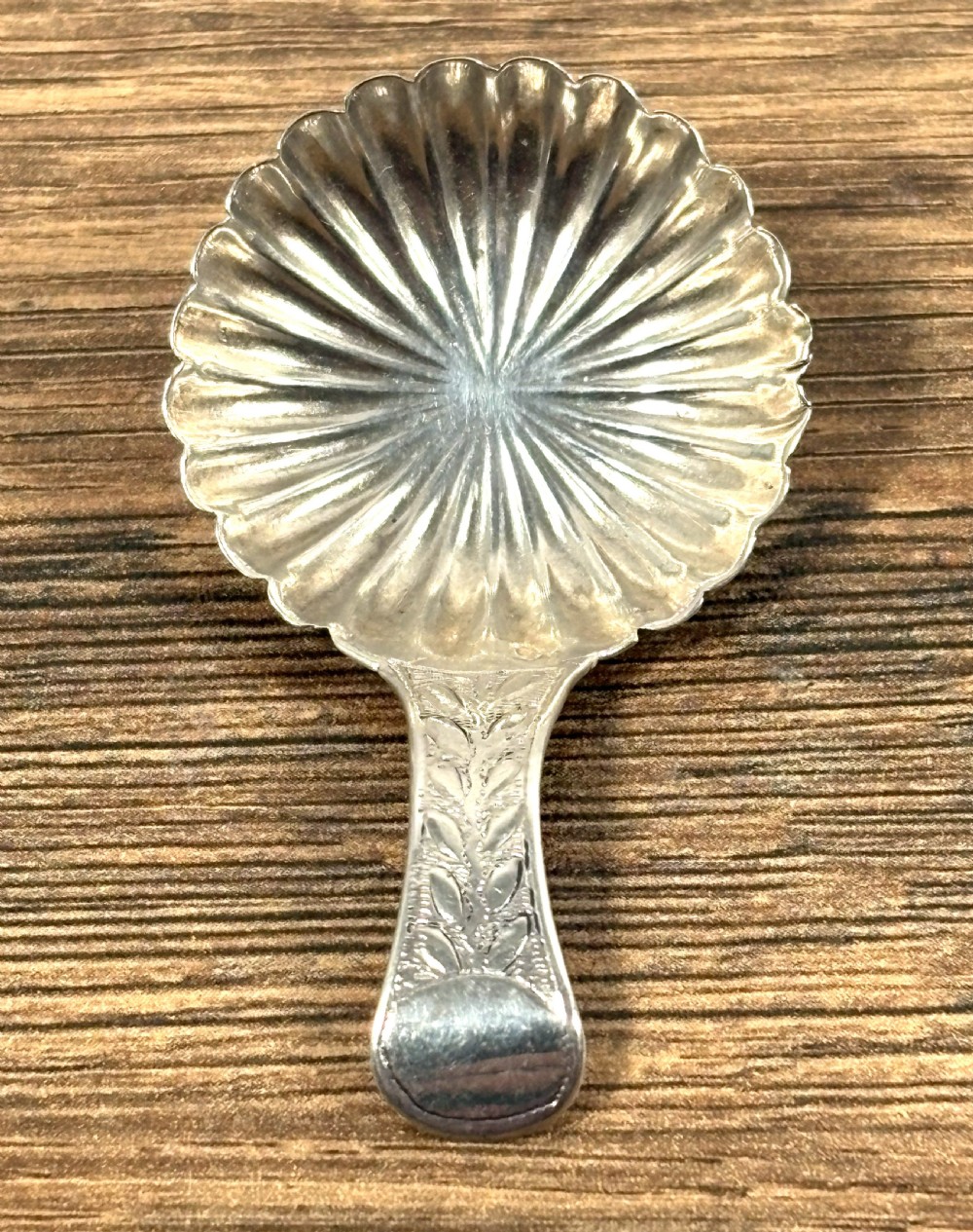 A Georgian sterling silver caddy spoon featuring a fluted shell-shaped bowl and an engraved leaf-pattern handle.