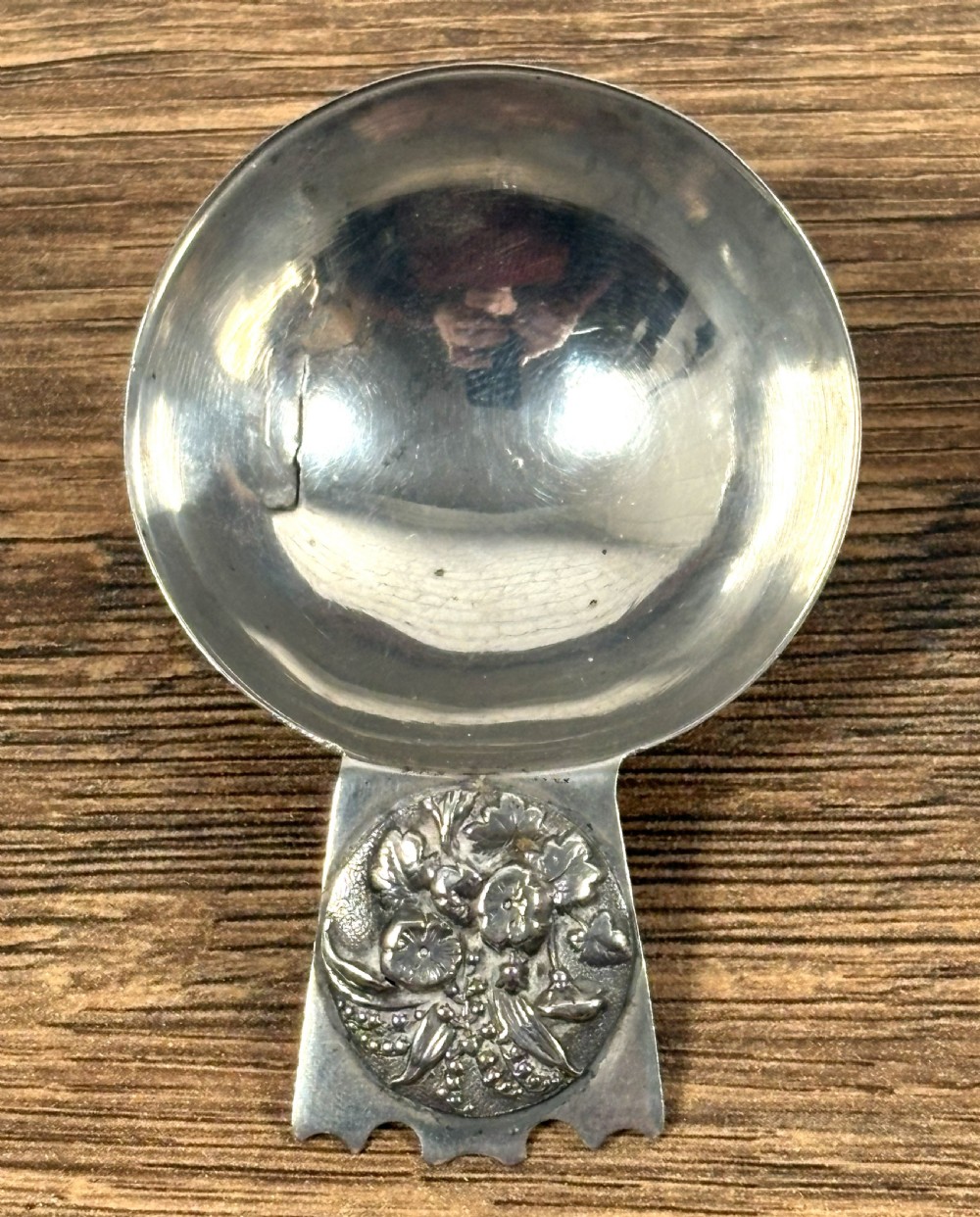 An Edwardian sterling silver caddy spoon featuring a smooth circular bowl and a short flat handle decorated with embossed floral detail. View II