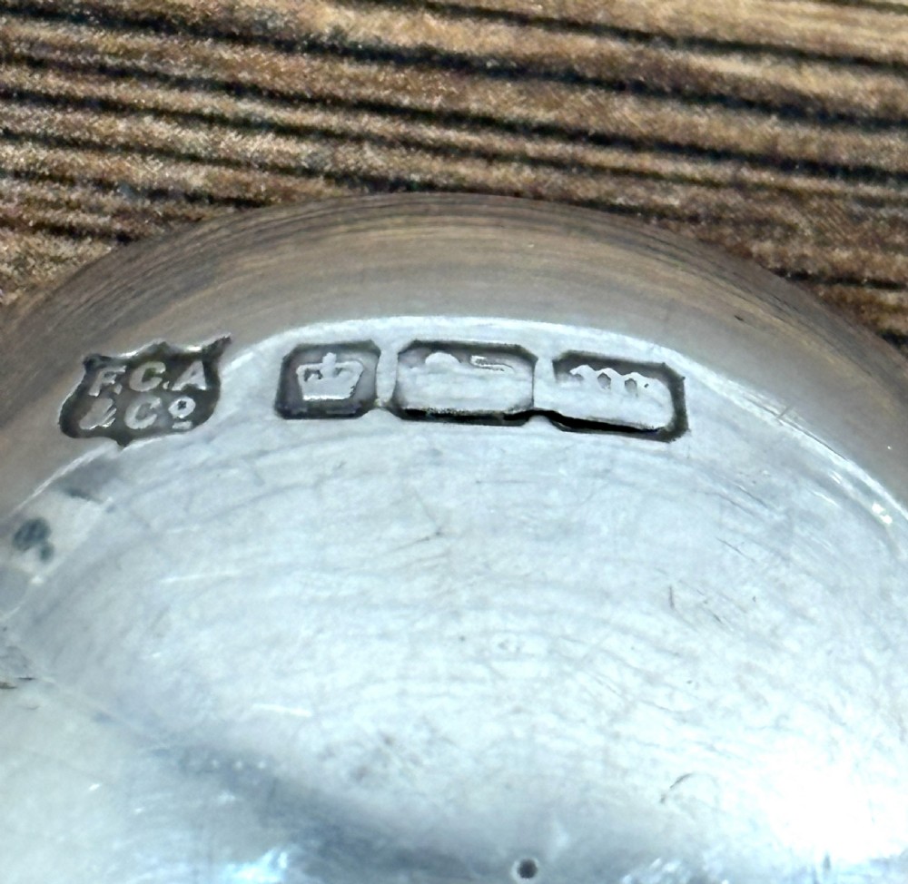 An Edwardian sterling silver caddy spoon featuring a smooth circular bowl and a short flat handle decorated with embossed floral detail. View V