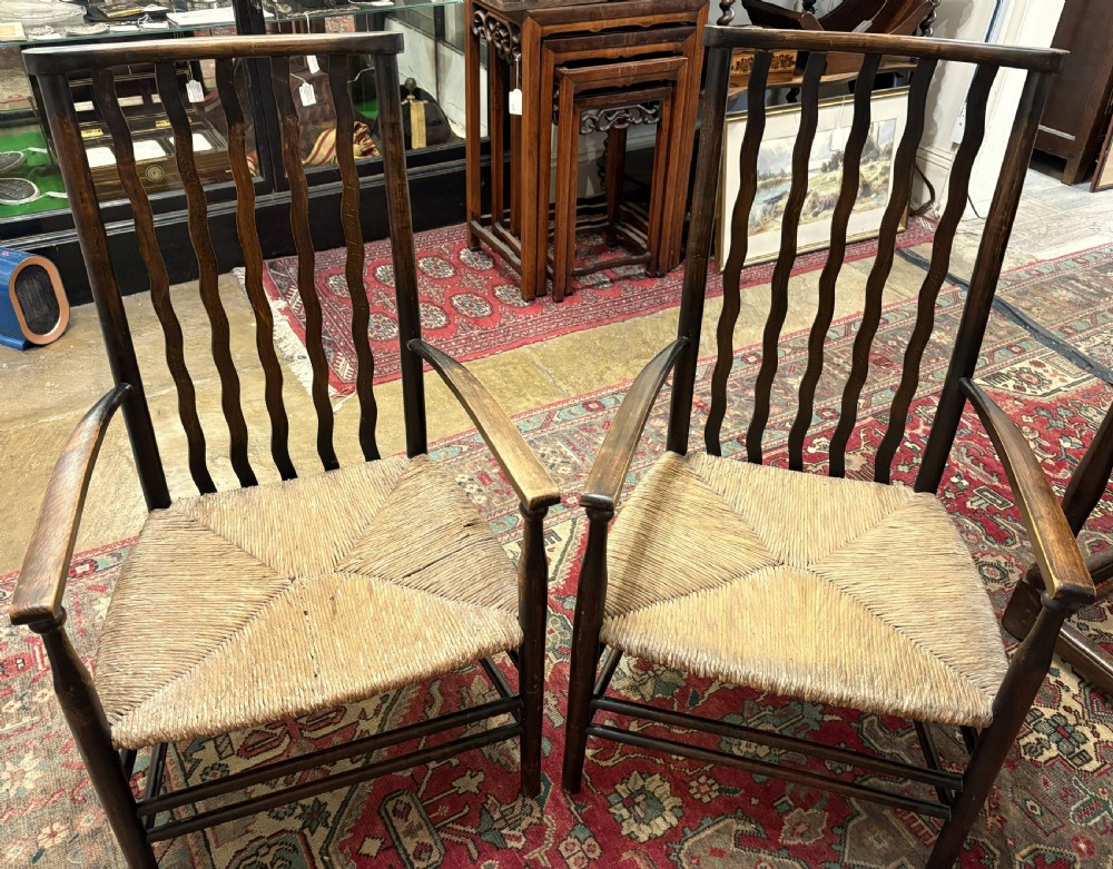 A pair of antique Arts and Crafts high-back dark wood armchairs featuring wavy back slats and woven natural rush seats.