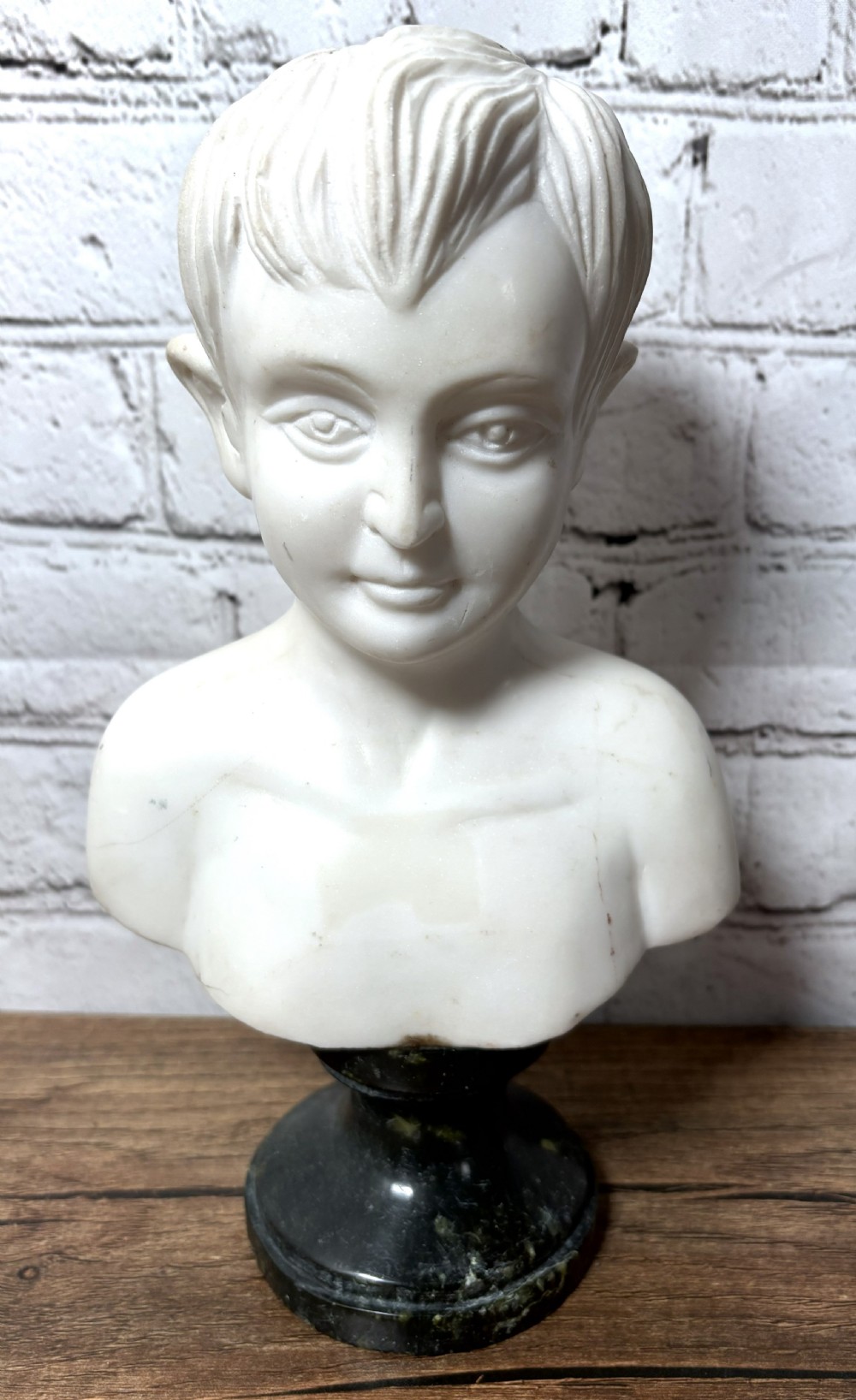 Carved white marble portrait bust depicting a young boy, raised on a dark green turned marble socle base.