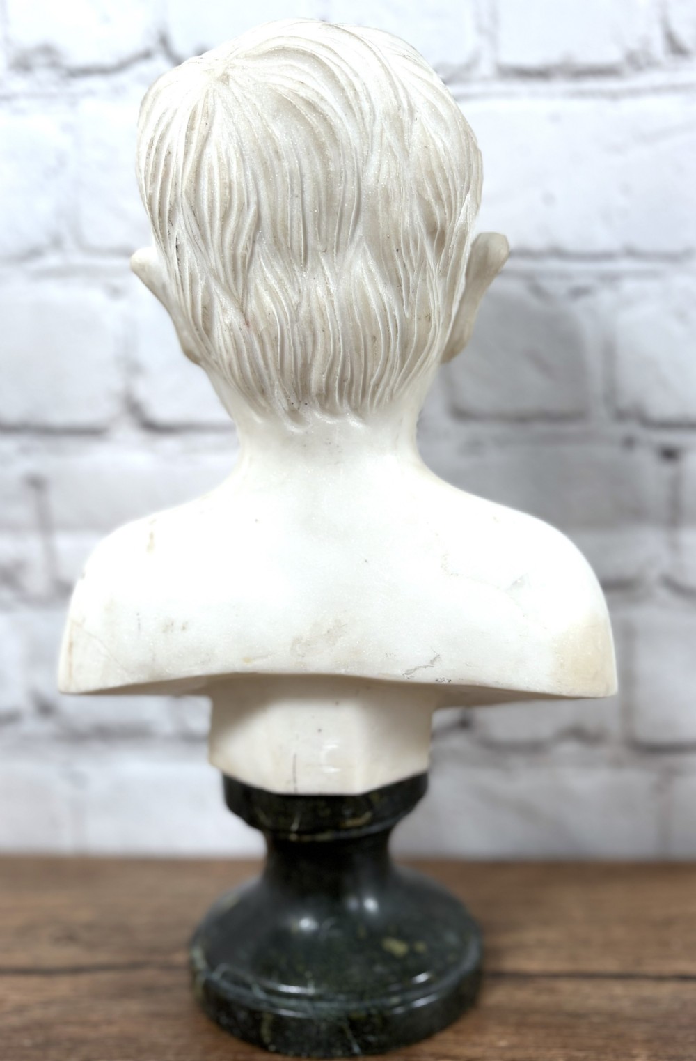Carved white marble portrait bust depicting a young boy, raised on a dark green turned marble socle base. View IV