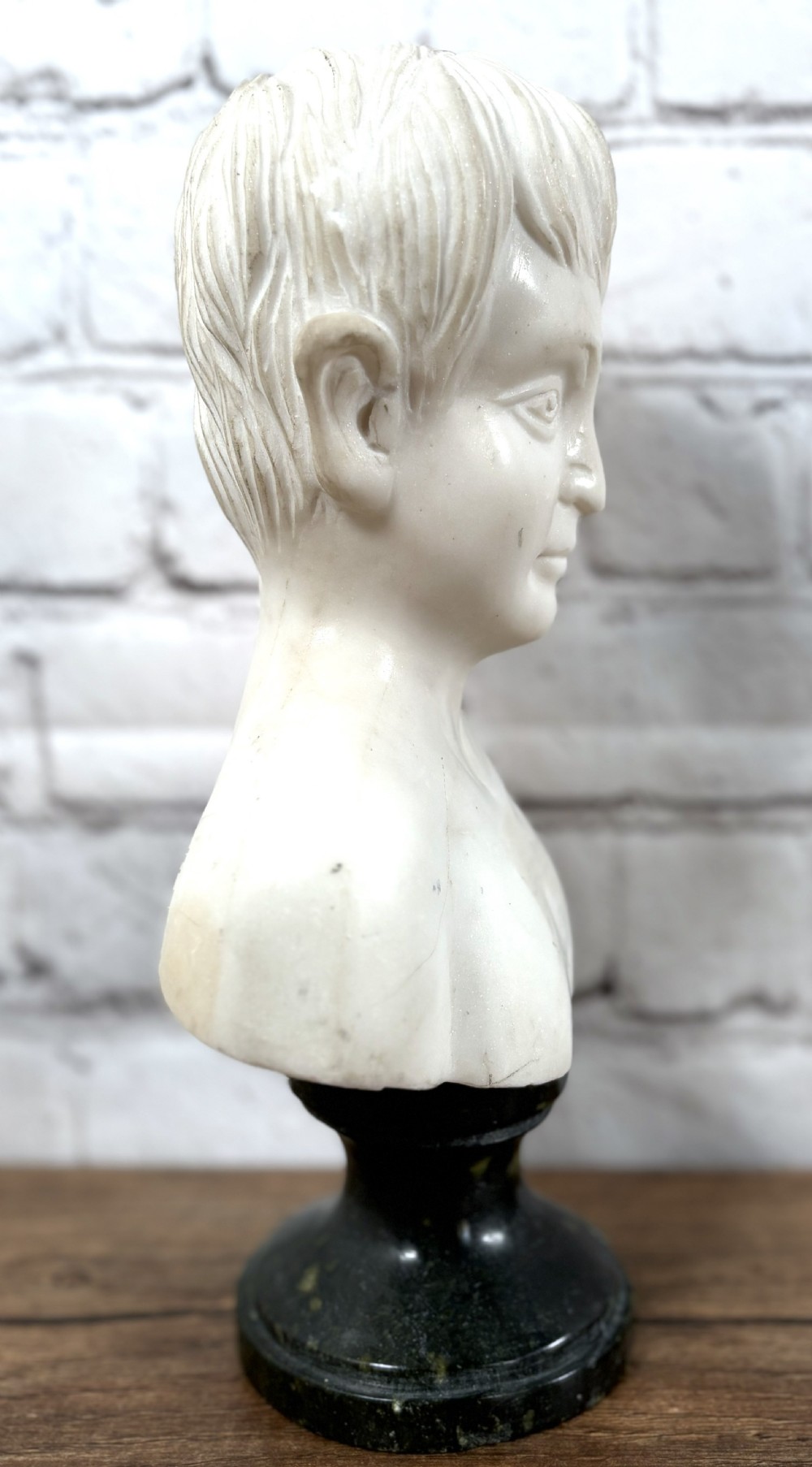 Carved white marble portrait bust depicting a young boy, raised on a dark green turned marble socle base. View V