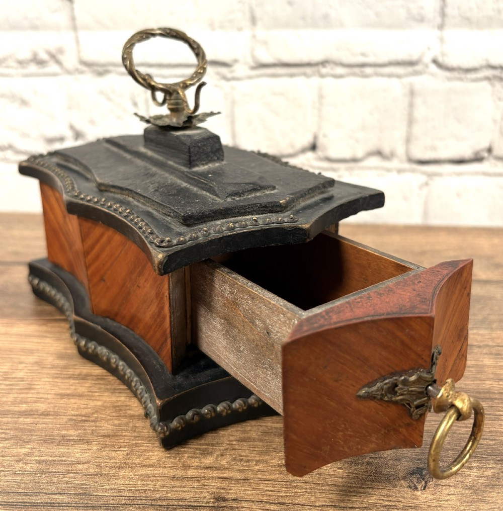 A 19th-century French kingwood trinket box featuring a serpentine ebonised base, parquetry wood veneer, and brass handles with a partially open drawer.