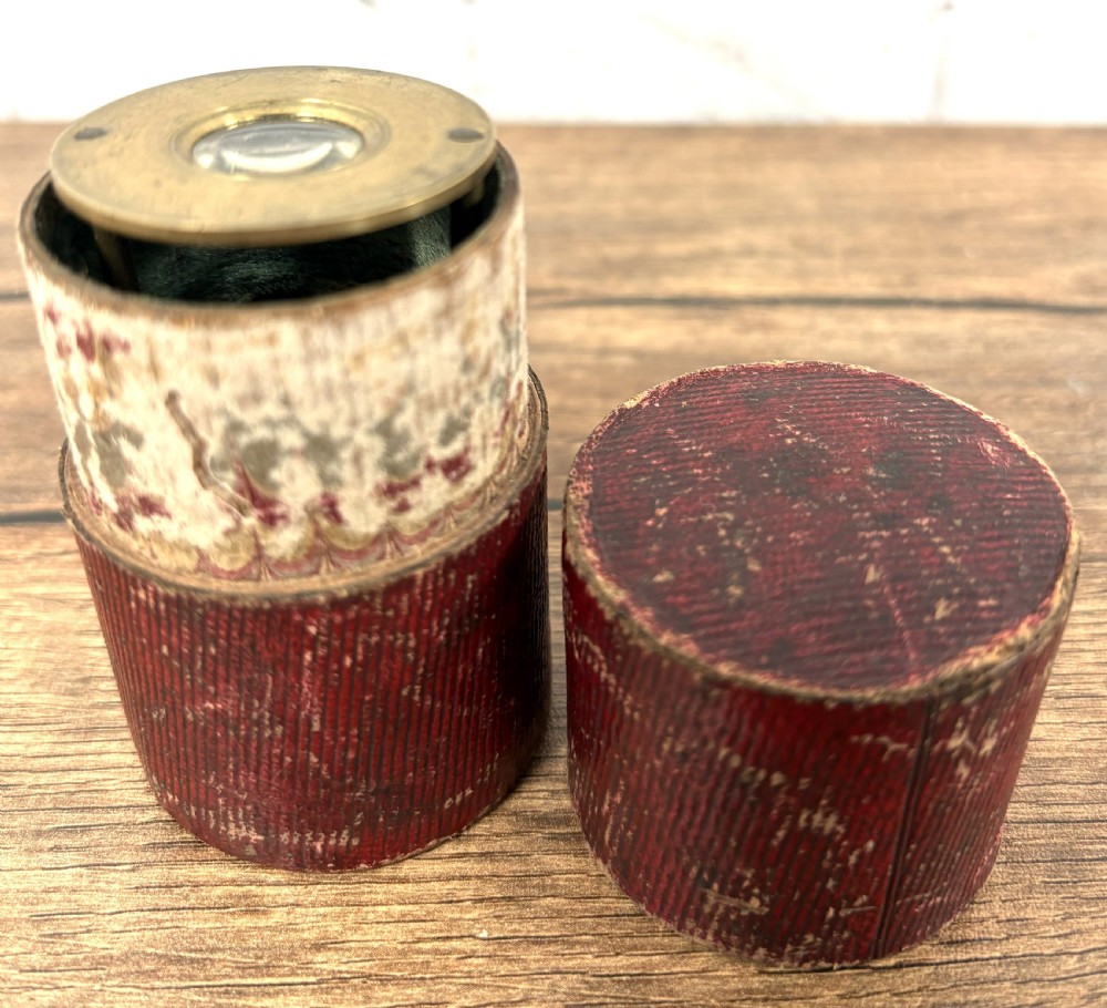 A Georgian brass travelling botanical microscope featuring three circular stages alongside its original red textured leather cylindrical case. View IV