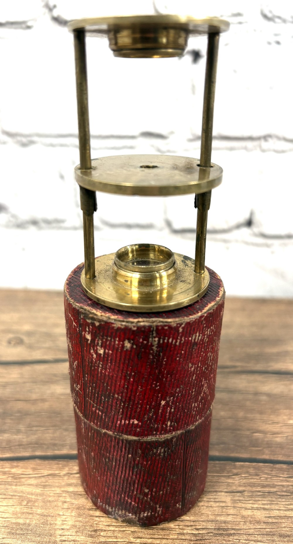 A Georgian brass travelling botanical microscope featuring three circular stages alongside its original red textured leather cylindrical case. View V