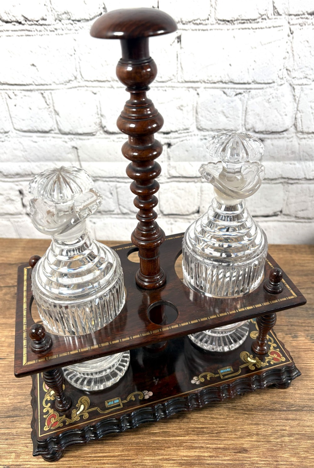 A Victorian dark rosewood decanter stand featuring decorative marquetry inlay, a turned central handle, and two cut glass decanters with faceted stoppers.