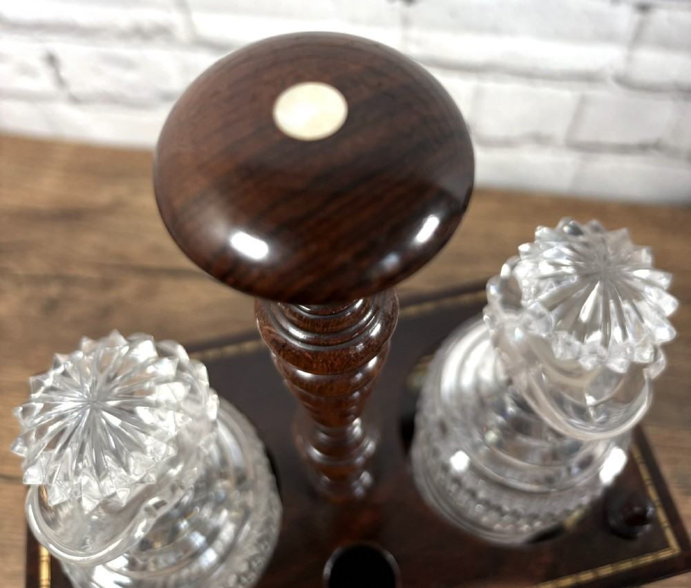 A Victorian dark rosewood decanter stand featuring decorative marquetry inlay, a turned central handle, and two cut glass decanters with faceted stoppers. View II