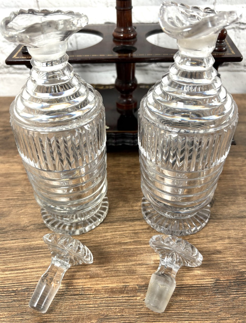 A Victorian dark rosewood decanter stand featuring decorative marquetry inlay, a turned central handle, and two cut glass decanters with faceted stoppers. View VI