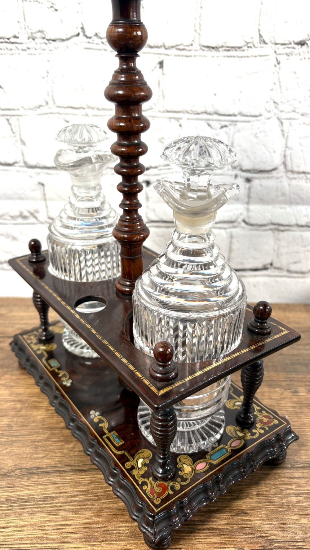 A Victorian dark rosewood decanter stand featuring decorative marquetry inlay, a turned central handle, and two cut glass decanters with faceted stoppers. View X