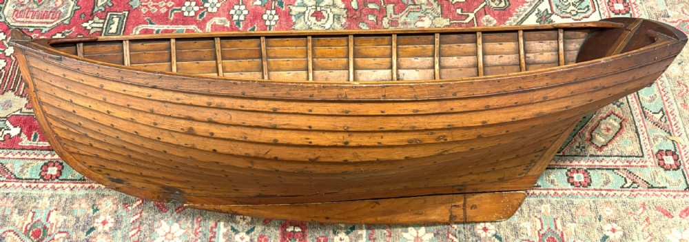 A nineteenth-century clinker-built wooden boat hull cradle with metal rivets and warm timber tones. View II