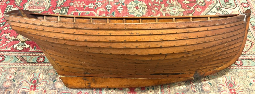 A nineteenth-century clinker-built wooden boat hull cradle with metal rivets and warm timber tones. View III