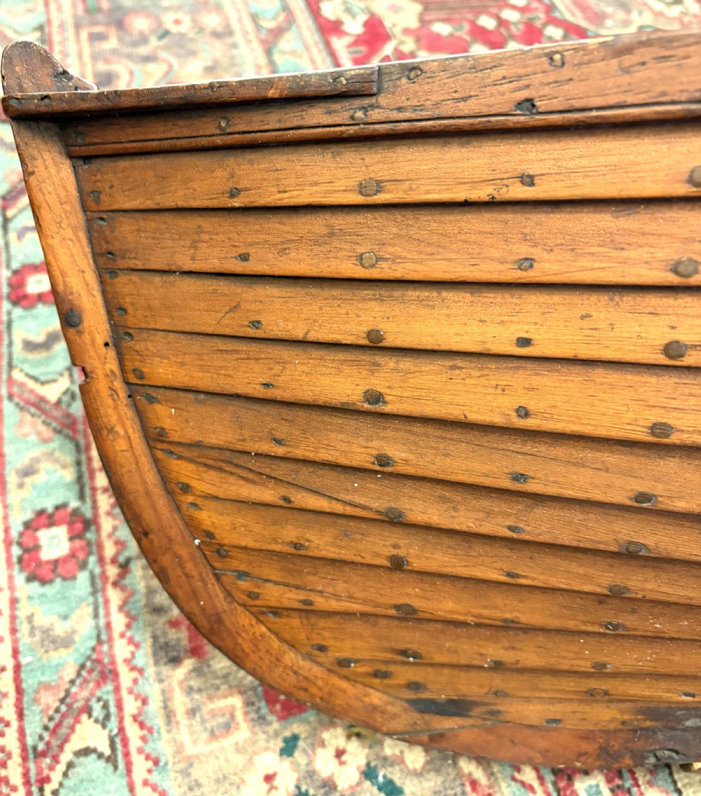 A nineteenth-century clinker-built wooden boat hull cradle with metal rivets and warm timber tones. View V