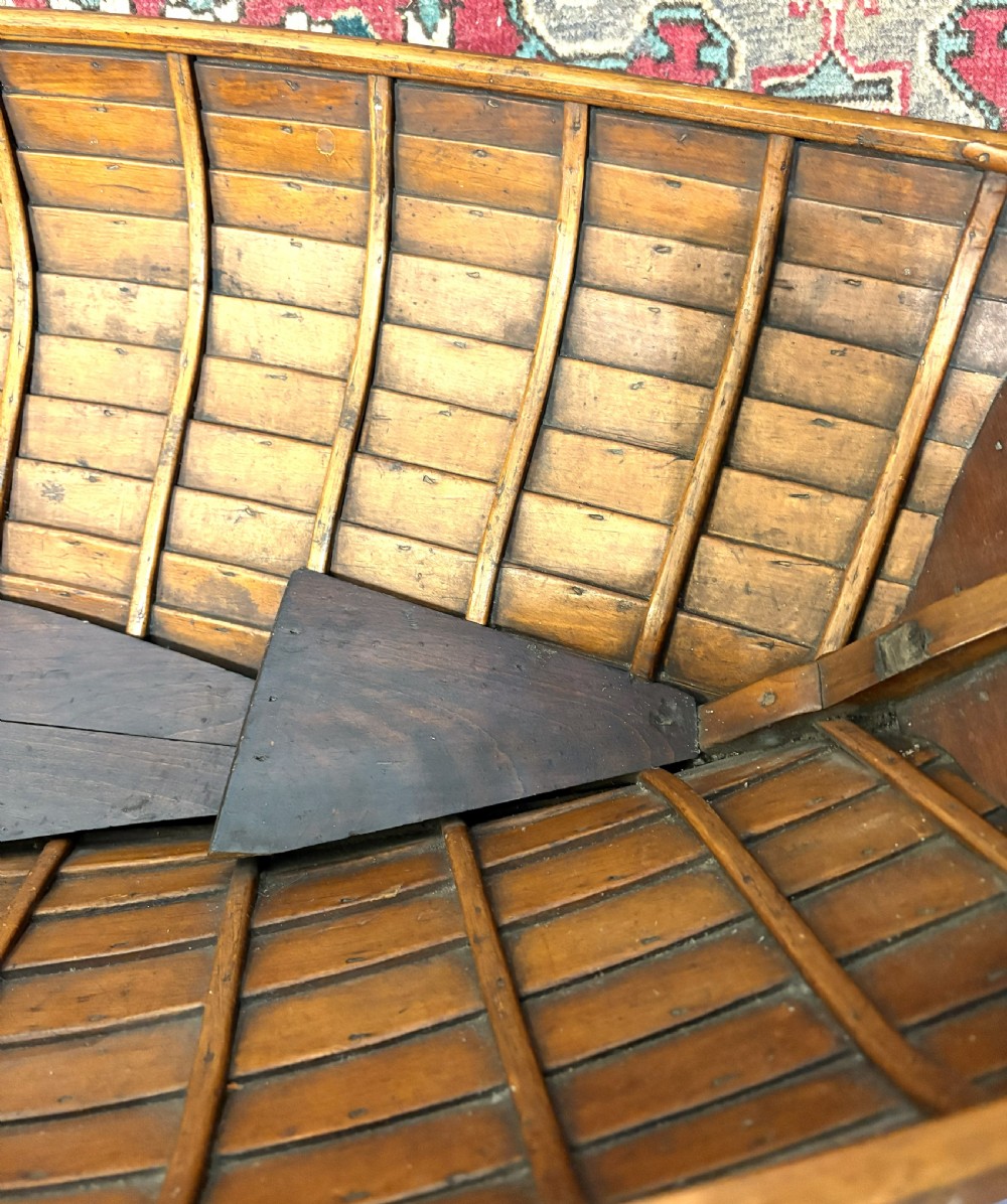 A nineteenth-century clinker-built wooden boat hull cradle with metal rivets and warm timber tones. View VII