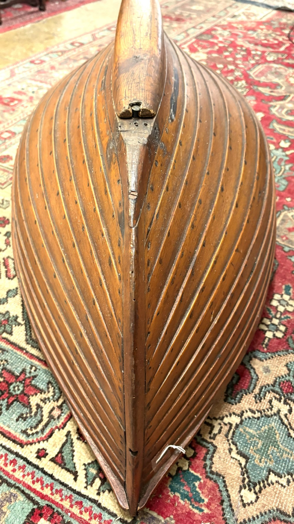 A nineteenth-century clinker-built wooden boat hull cradle with metal rivets and warm timber tones. View X