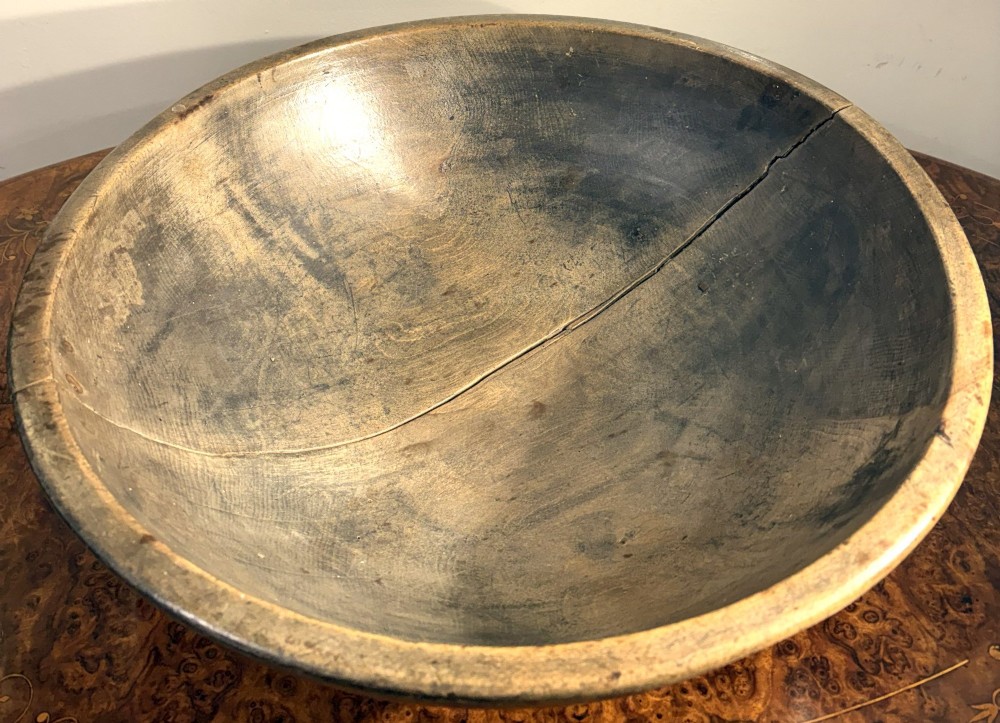 An eighteenth-century hand-turned sycamore wooden bowl displaying a weathered dark grey patina and an authentic historic timber split line.