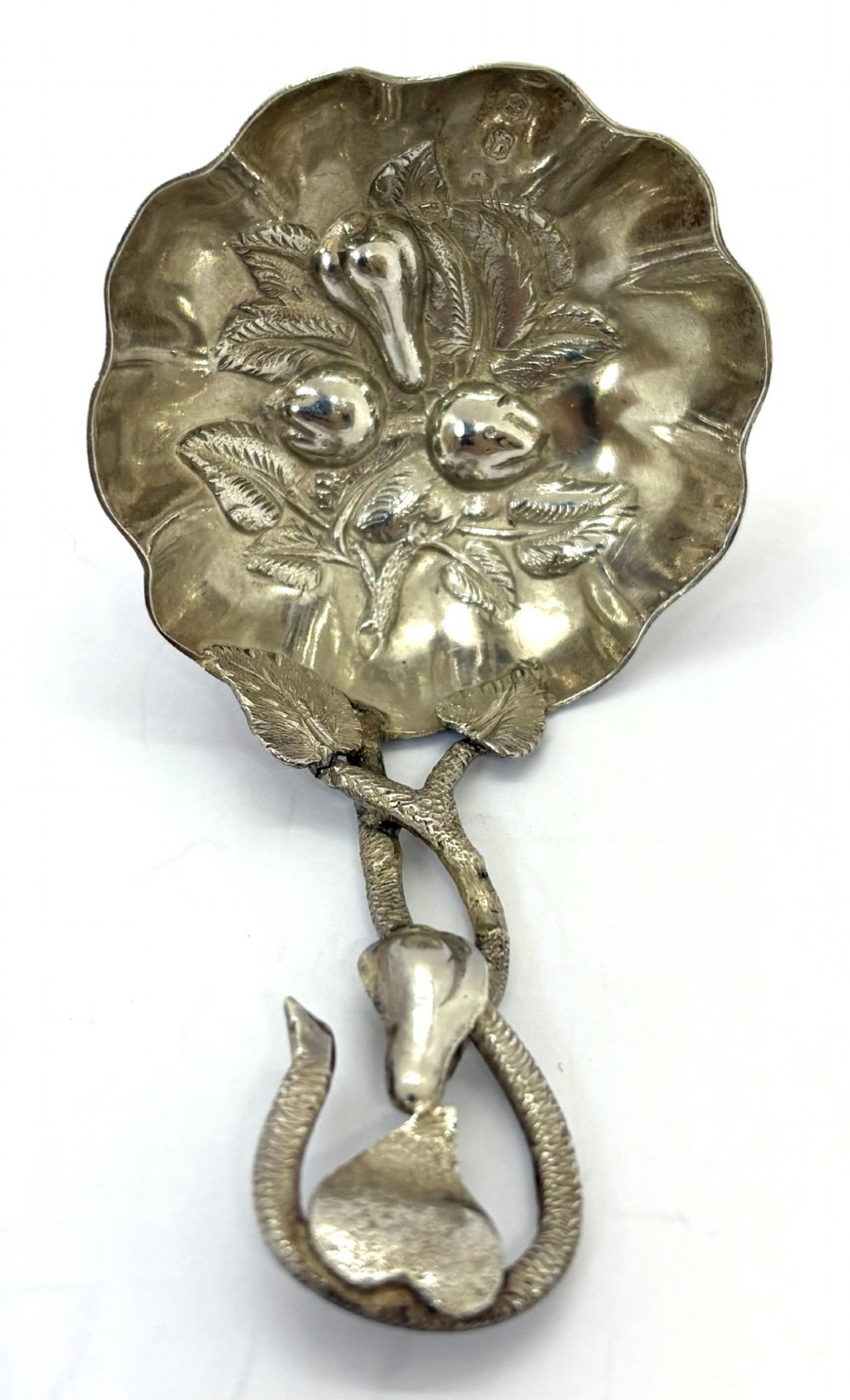 A Victorian silver caddy spoon featuring a scalloped bowl embossed with fruit and leaves alongside a branch-form handle.