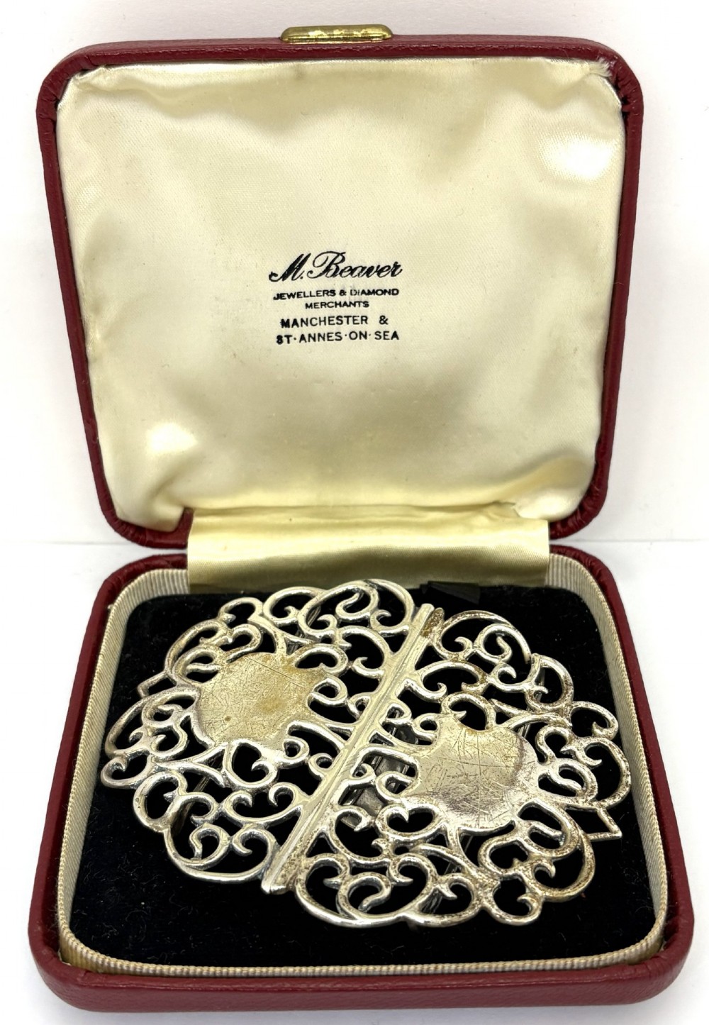 A two-piece pierced silver belt buckle with intricate scrollwork detailing, presented inside its original silk-lined presentation box.