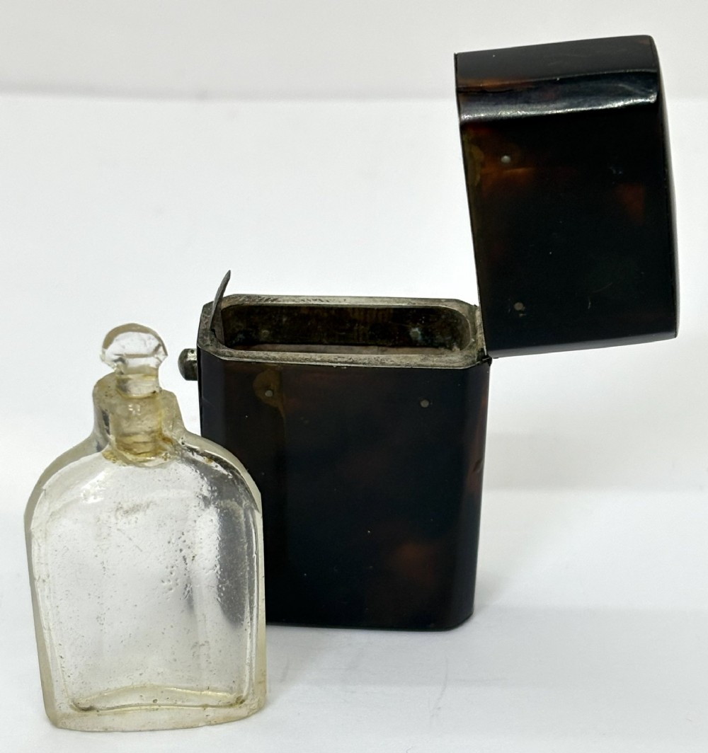 A small Georgian hinged tortoiseshell case shown open beside its matching clear glass scent bottle with a glass stopper.