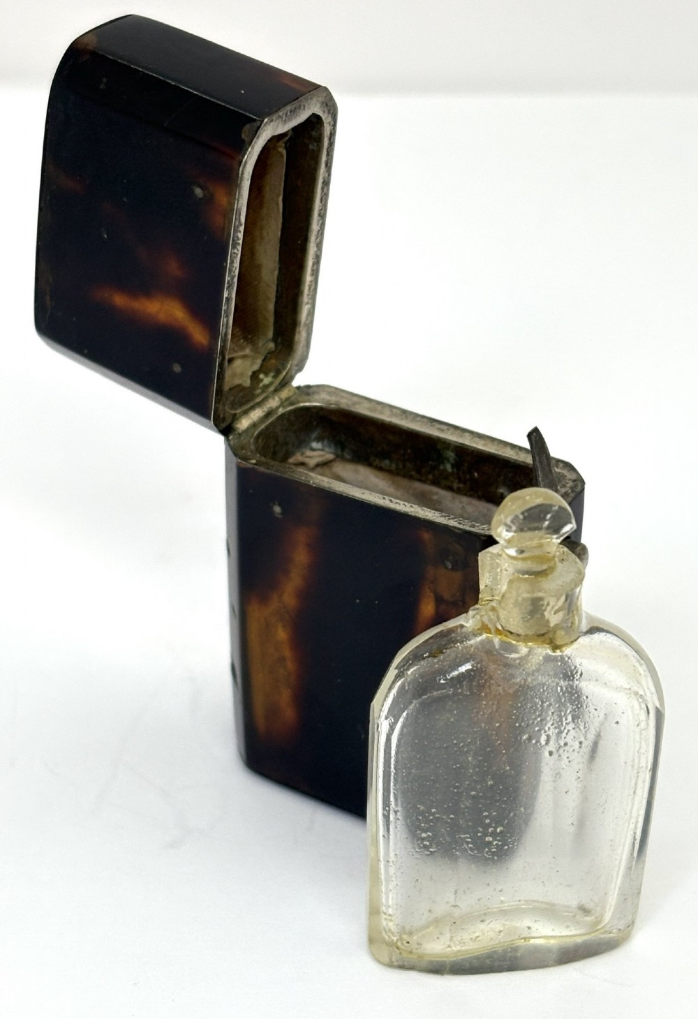 A small Georgian hinged tortoiseshell case shown open beside its matching clear glass scent bottle with a glass stopper. View IV